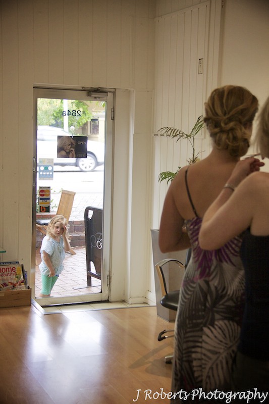 Little girl looking in window at bride having hair and make up applied - wedding photography sydney